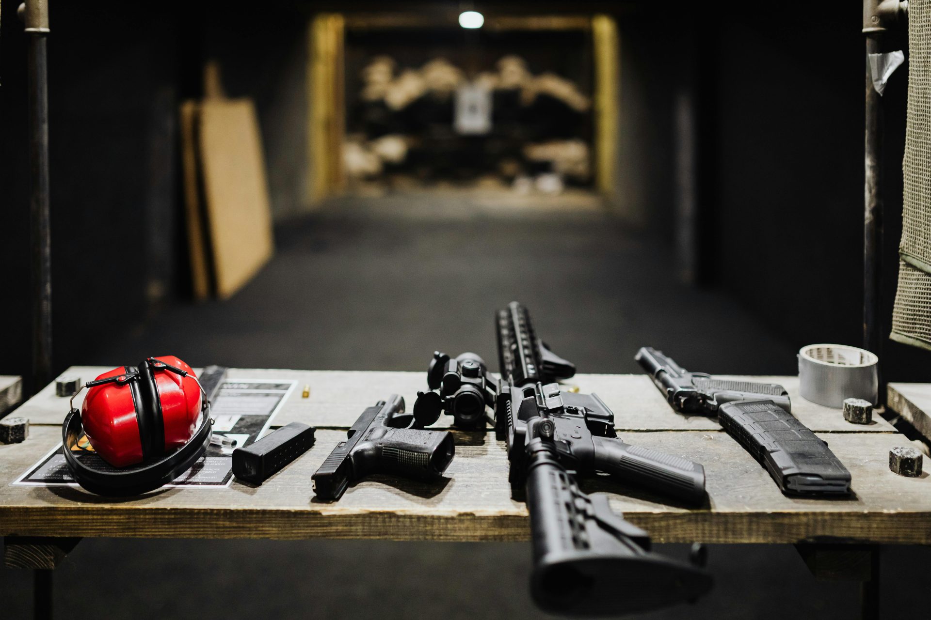 Verschiedene Schusswaffen auf einem Holztisch in einem Indoor-Schießstand angeordnet.